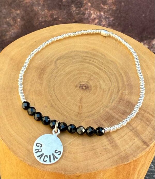 pulsera elasticada con medalla diseño gracias hecha de plata 950, mostacillas de plata 1000 y piedras turmalina negra