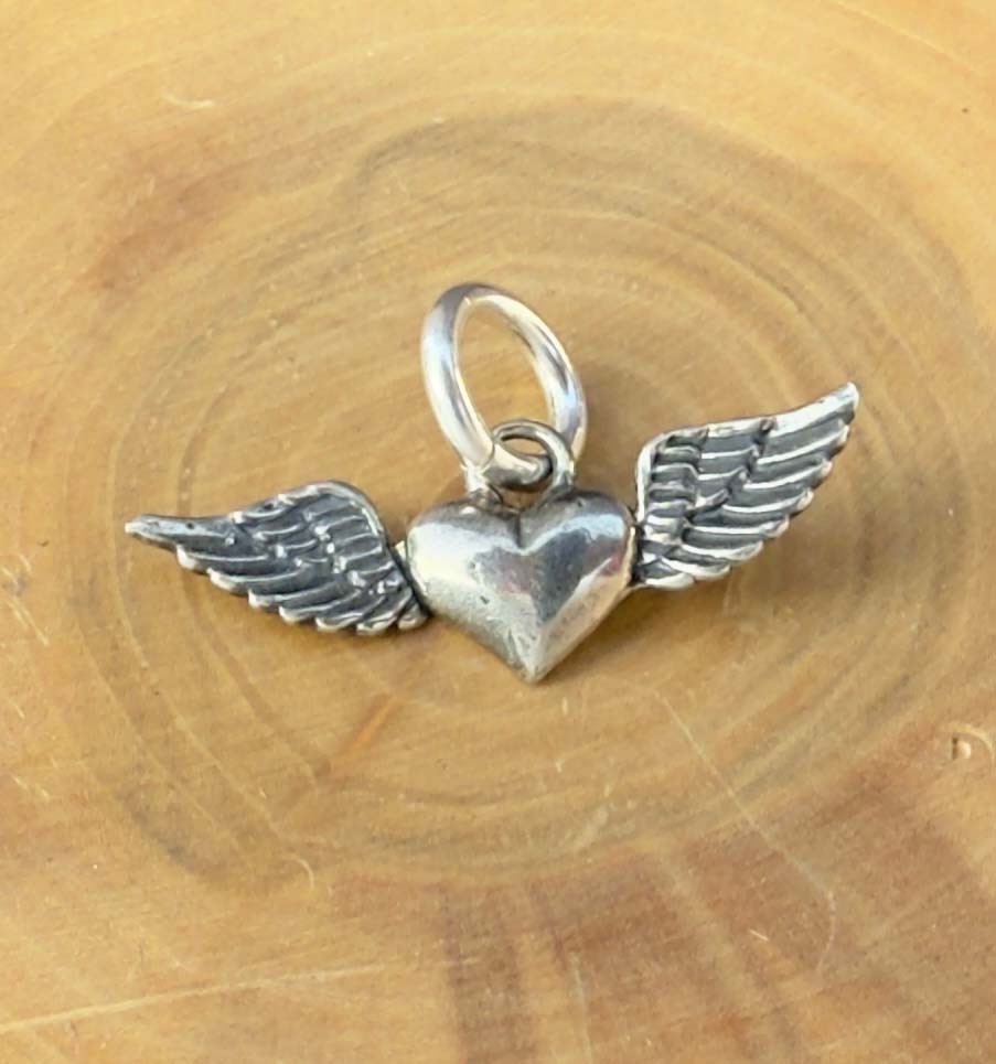 medalla hecha de plata 950 con diseño de corazon con alas en sus costados.