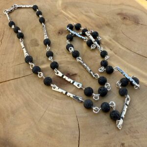 cadena de plata formada por perfiles, tambien de plata, grabada con zurcos triangulares y acompañadas de piedras volcanicas antorchadas unidas a los perfiles por un alambre de plata.