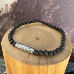 Pulsera elasticada formada por un tubo delgado de plata con texturas de lineas martilladas. Acompañado de mostacillas de piedra volcanica.