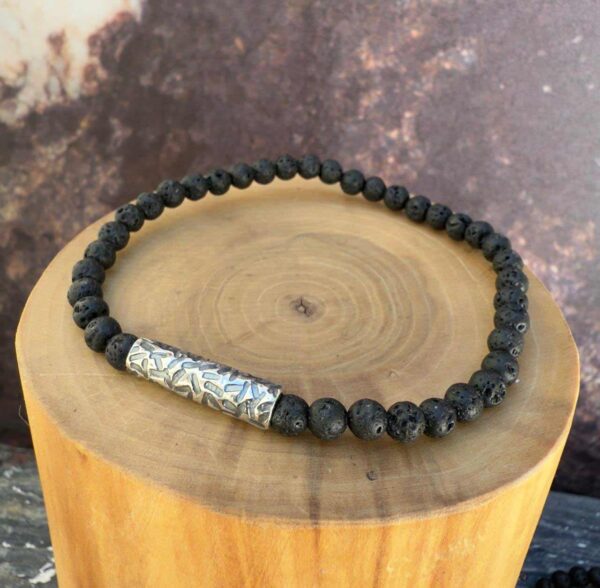 Pulsera elasticada formada por un tubo delgado de plata con texturas de lineas martilladas. Acompañado de mostacillas de piedra volcanica.