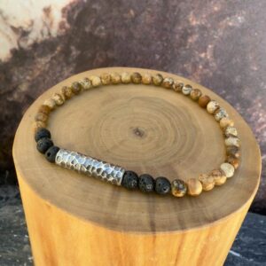 Pulsera elasticada formada con un tubo central de plata estriada acompañado de mostacillas de piedra volcanica negra y jaspe amarillo