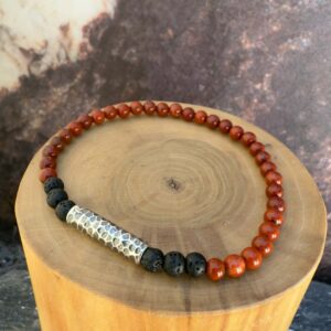 Pulsera elasticada formada con un tubo central de plata martillada acompañado de mostacillas de piedra volcanica negra y jaspe rojo