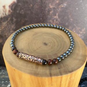 Pulsera elasticada formada con un tubo central de cobre martillado rodeado por piedras ojo de buey, acompañado de mostacillas de 4 milímetros de diámetro de hematita y ojo de buey