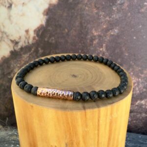 Pulsera elasticada formada con un tubo central de cobre martillado, acompañado de mostacillas de 4 milímetros de diámetro de piedra volcanica negra