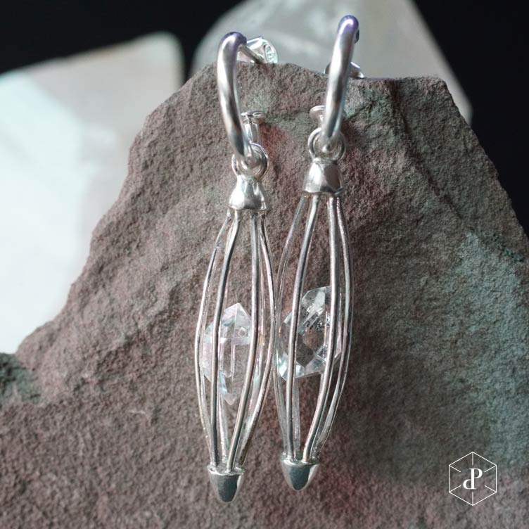 aros con diseño de jaula ovalada hecha de p´lata 950 que dentro sostiene un cuarzo diamante herkimer de 5 centimetros