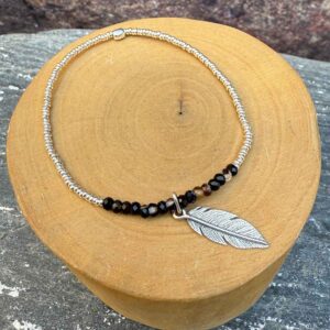 pulsera elasticada con mostacillas de onix y plata 1000, con medalla de diseño de pluma hecha de plata 950