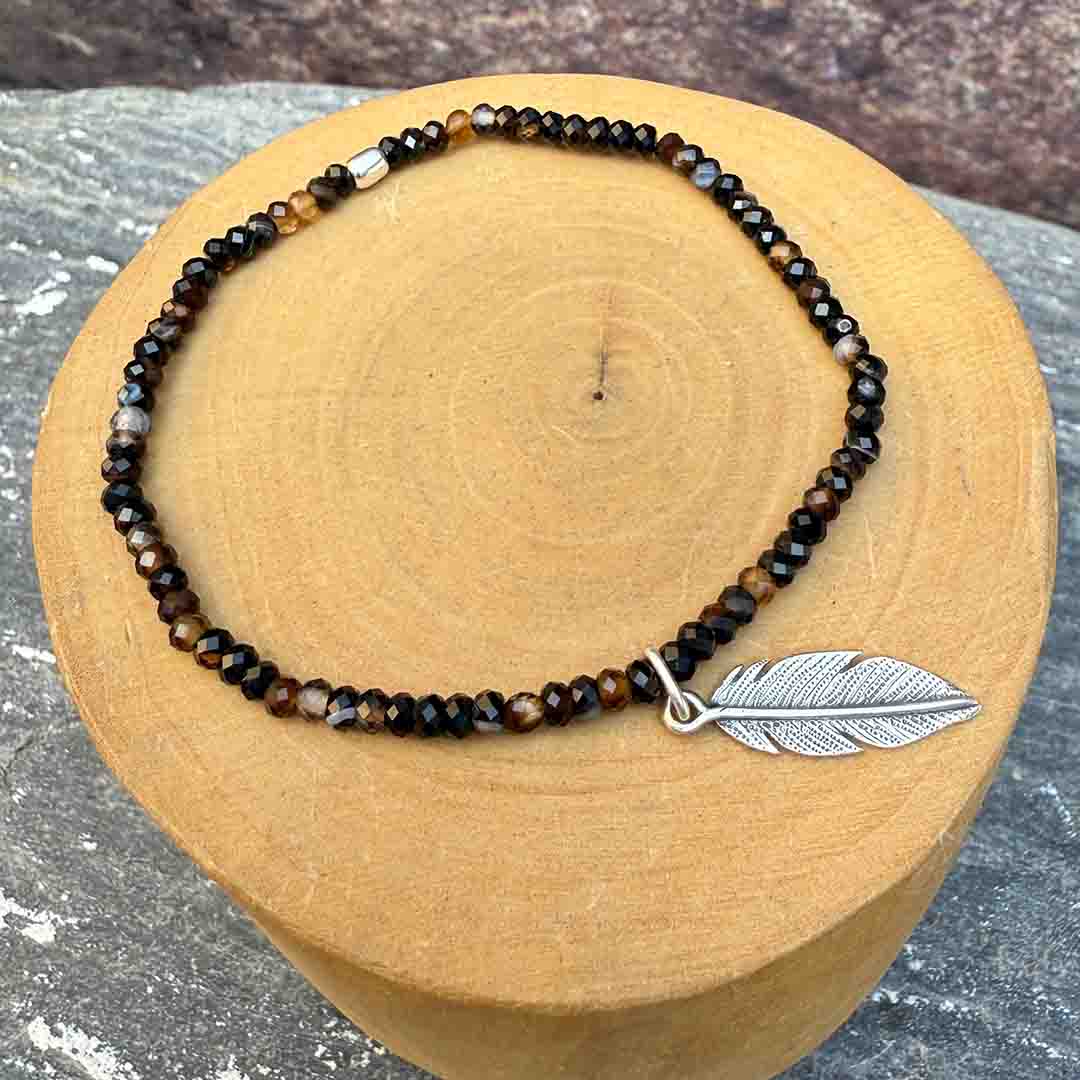 pulsera elasticada con mostacillas de onix, con medalla de diseño de pluma hecha de plata 950