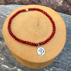 pulsera elasticada con mostacillas de cristal rojo, con una medalla central de plata 950 con simbolo OM