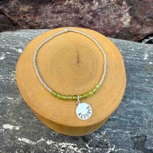 pulsera elasticada con mostacillas de peridoto y plata 1000, con medalla circular con la palabra alegria grabada, hecha de plata 950