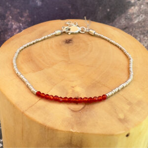 pulsera de plata hecha con mostacillas de cristal rojo posada sobre un tronco de madera