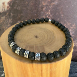 Pulsera elasticada formada con un centro de mostacillas anchas de plata texturizada con estrias interlineadas con mostacillas de piedra volcanica negra en su centro y extremos.