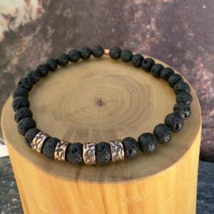 Pulsera elasticada formada con un centro mostacillas de cobre con texturas de lineas martilladas interlineadas con mostacillas de piedra volcanica negra