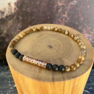 Pulsera elasticada formada con un tubo central de cobre martillado, acompañado de mostacillas de 4 milímetros de diámetro de piedra volcanica negra y jaspe amarillo